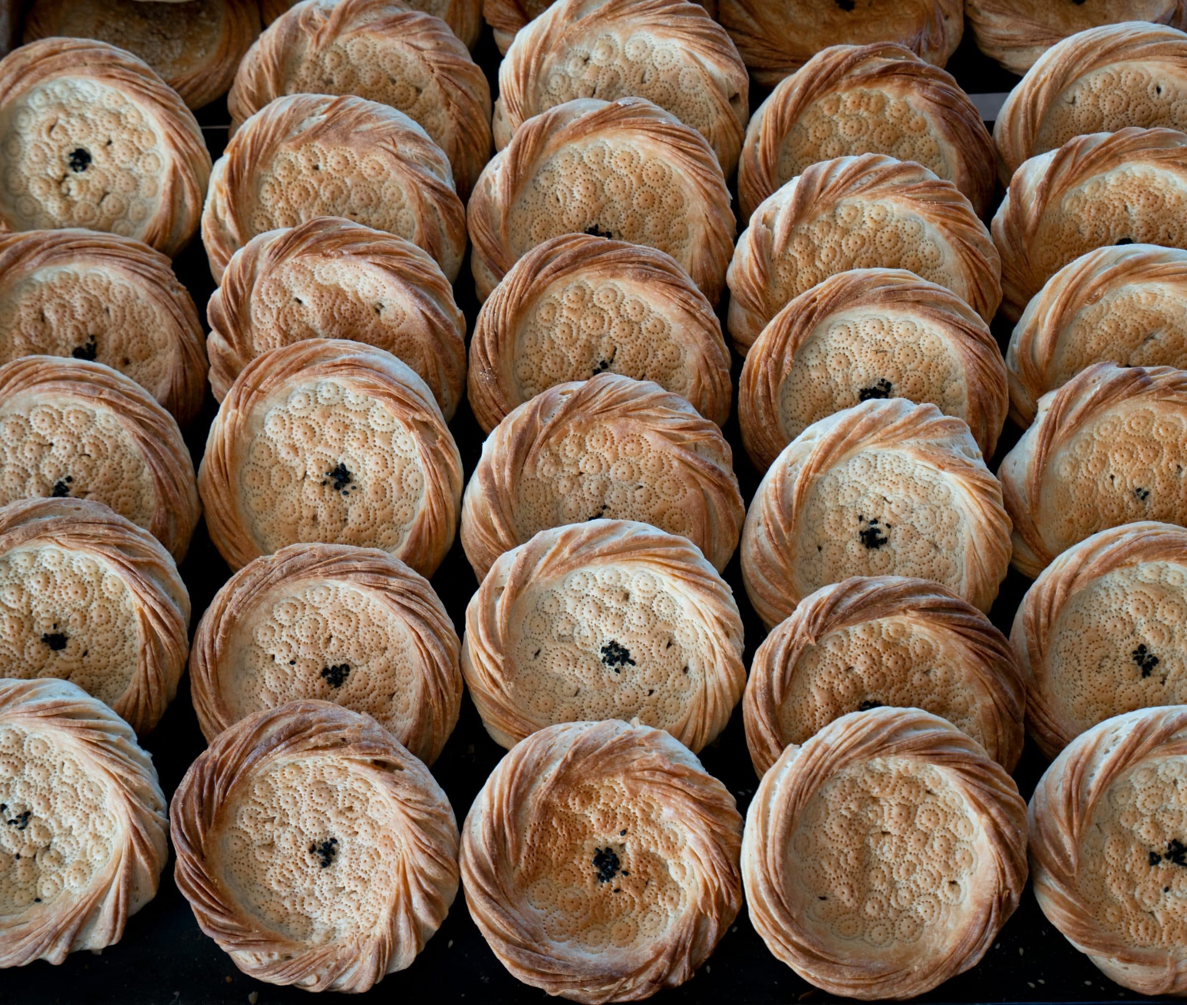 Rounds of Uzbek non stacked in rows at a bazaar stall.